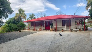 A house with a red roof and white walls, surrounded by greenery and a concrete driveway.