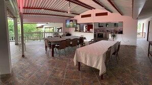 A spacious dining area with a large table and chairs, a kitchen area with cabinets and a countertop, and a balcony with a railing.
