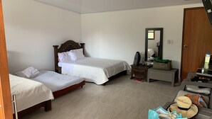 A hotel room with two single beds, a wooden nightstand, a mirror, and a wicker chair with a hat and a bag.