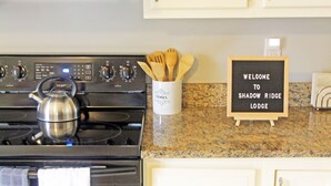 A kitchen with white cabinets, a stainless steel stove, a kettle, and a welcome sign. - Mountain Views & Solitude. This is Shadow Ridge. Hot Tub. (Fletcher)