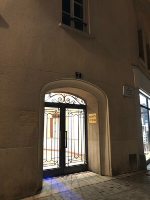 A building entrance with a wrought iron gate, a small sign above the door, and a number '7' sign on the wall.