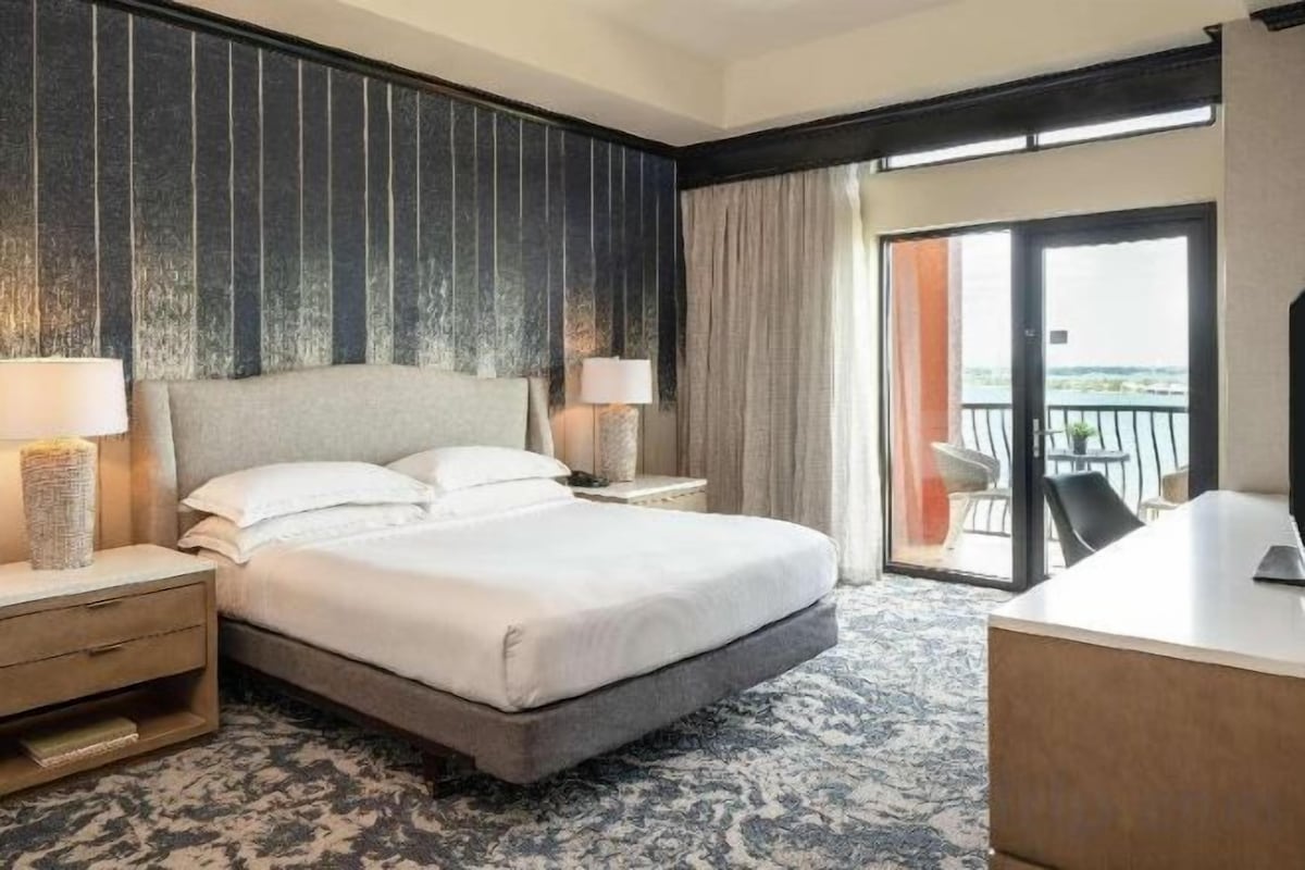 Habitación de hotel con una cama grande, dos mesitas de noche, un escritorio y un balcón con vistas.