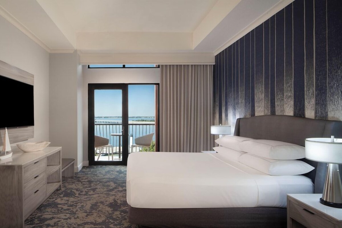 A hotel room with a bed, a TV, a desk, a chair, and a view of the outdoors.