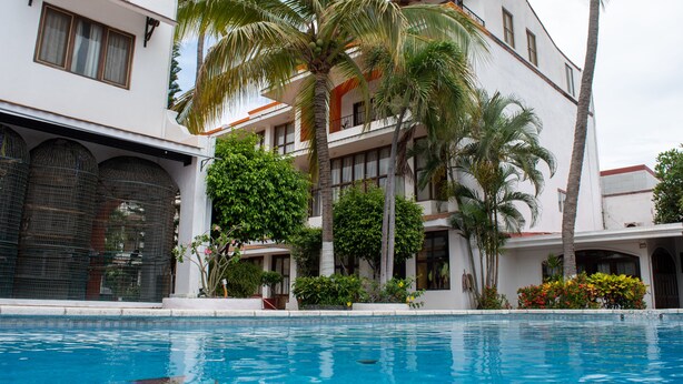 A poolside view of a hotel with a pool, palm trees, and a building with balconies. - Hotel Boutique La Pergola (Manzanillo)