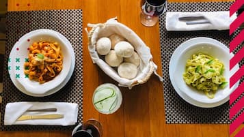 Una mesa de comedor con tres platos de pasta, una cesta de pan y un vaso de agua.