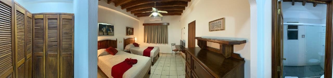 Habitación con dos camas, un escritorio, ventilador de techo y ventana con cortinas.