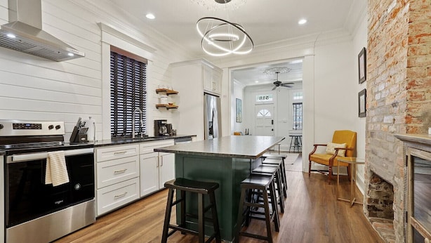 A modern kitchen with a central island, stainless steel appliances, and a brick accent wall. - Historic Shotgun, Near Streetcar and Superdome (New Orleans)