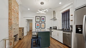 A modern kitchen with a central island, stainless steel appliances, and a brick accent wall. - Historic Shotgun, Near Streetcar and Superdome (New Orleans)