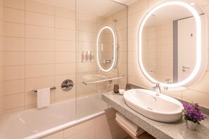 A modern bathroom with a bathtub, a sink, a mirror with a light, and toiletries on the wall.
