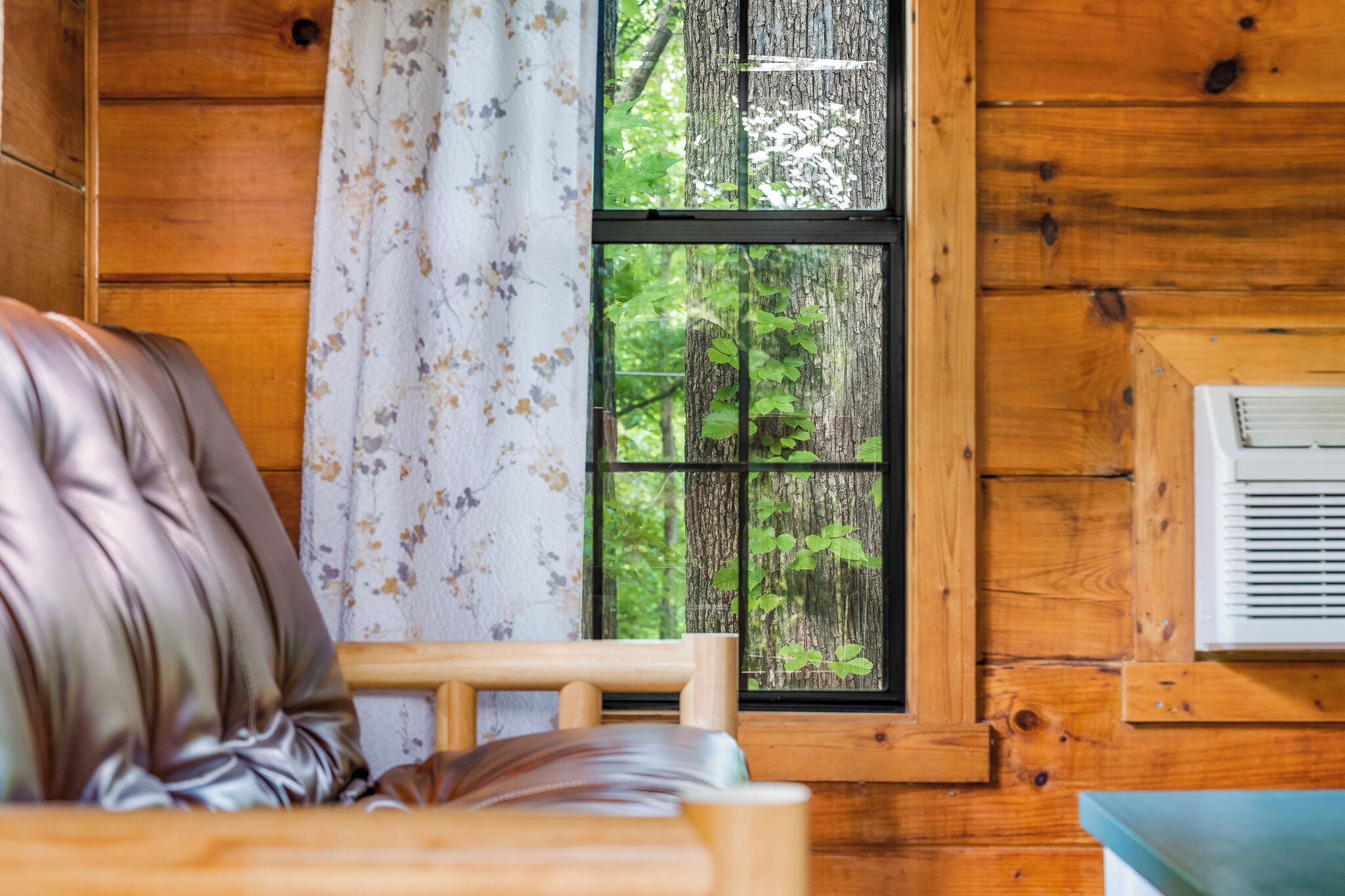 Une chambre dans un chalet en bois, avec un lit, une fenêtre donnant sur les arbres et un climatiseur fixé au mur.