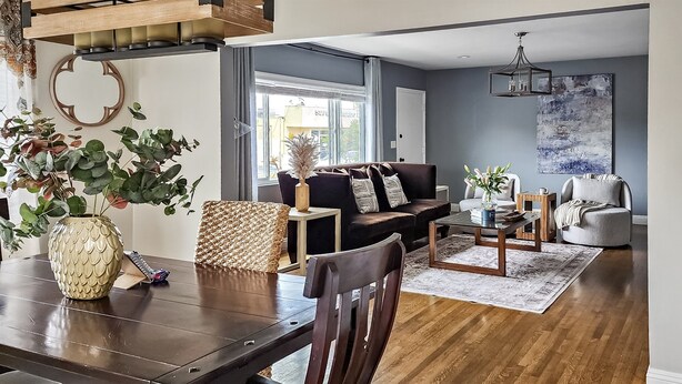 A modern living room with a dark brown sofa, a coffee table, and a dining table with chairs. There is a large window providing natural light, and a painting on the wall. - Spacious Apt. Min to Downtown Culver City & Venice Beach (Culver City)