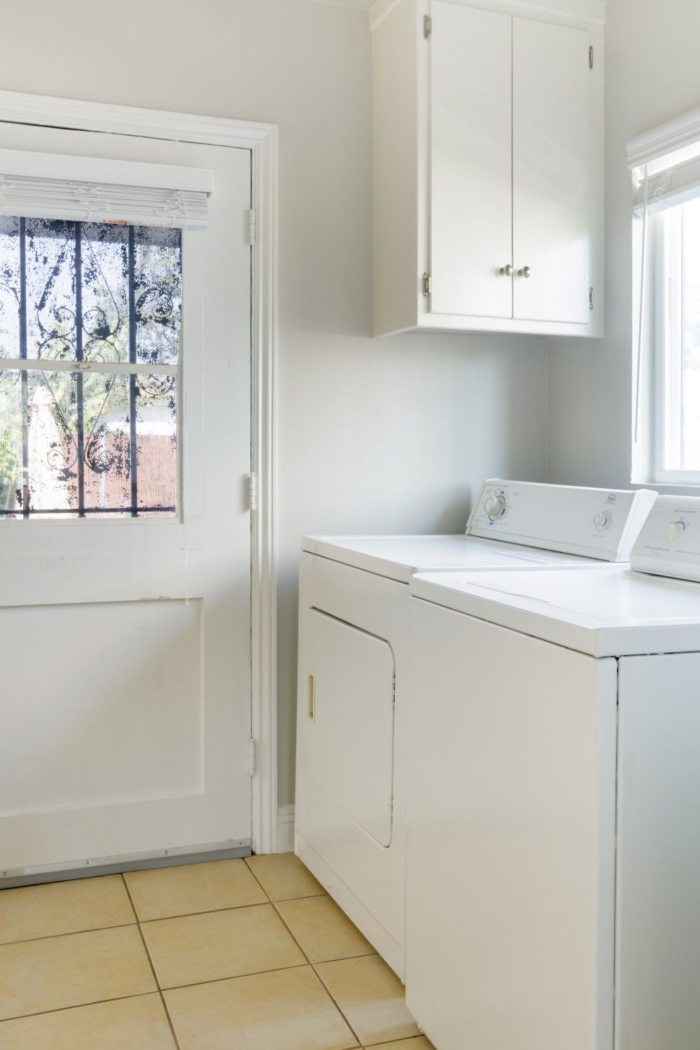 A laundry room with a washing machine and dryer, a white door, and a window with metal bars.