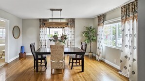 A dining area with a wooden table and chairs, a hanging light fixture, and patterned curtains. - Spacious Apt. Min to Downtown Culver City & Venice Beach (Culver City)
