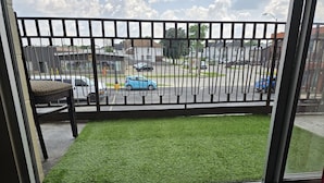 Un balcon avec du gazon synthétique, une chaise et une vue sur un parking rempli de voitures.