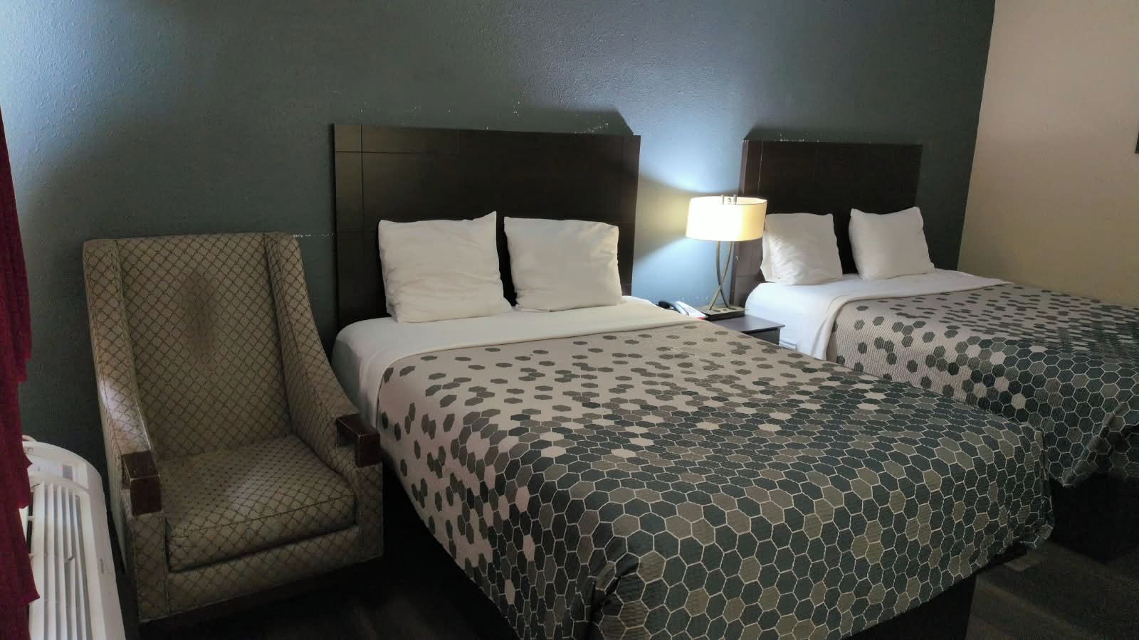 Ein Hotelzimmer mit zwei Betten, einem Sessel und einer Lampe.