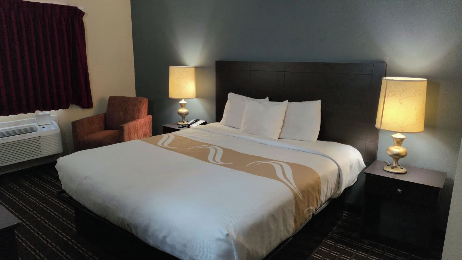 Een hotelkamer met een groot bed, twee bedlampen, een stoel en een verwarming.