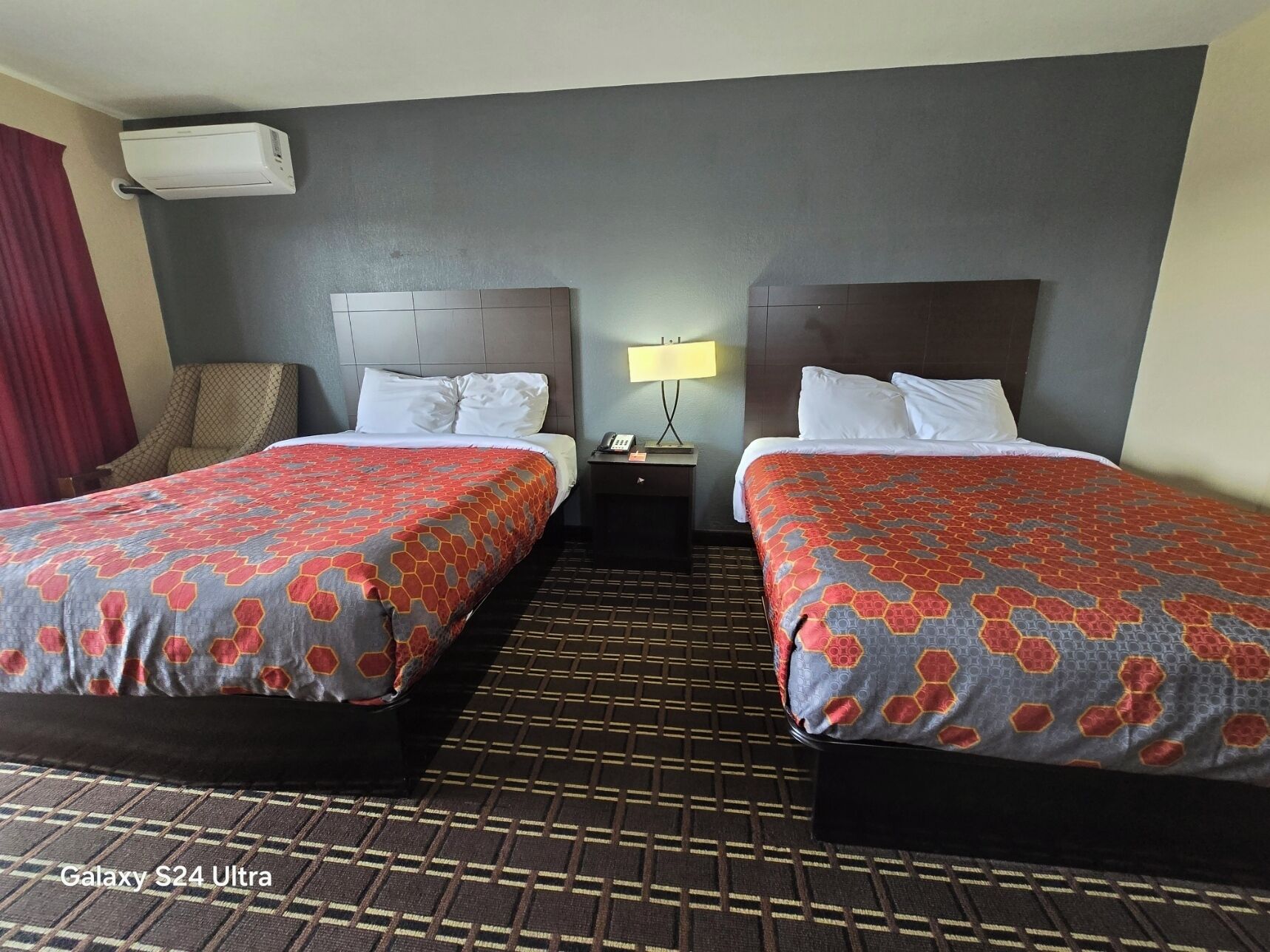 Habitación de hotel con dos camas, una mesita de noche con lámpara y un equipo de aire acondicionado.