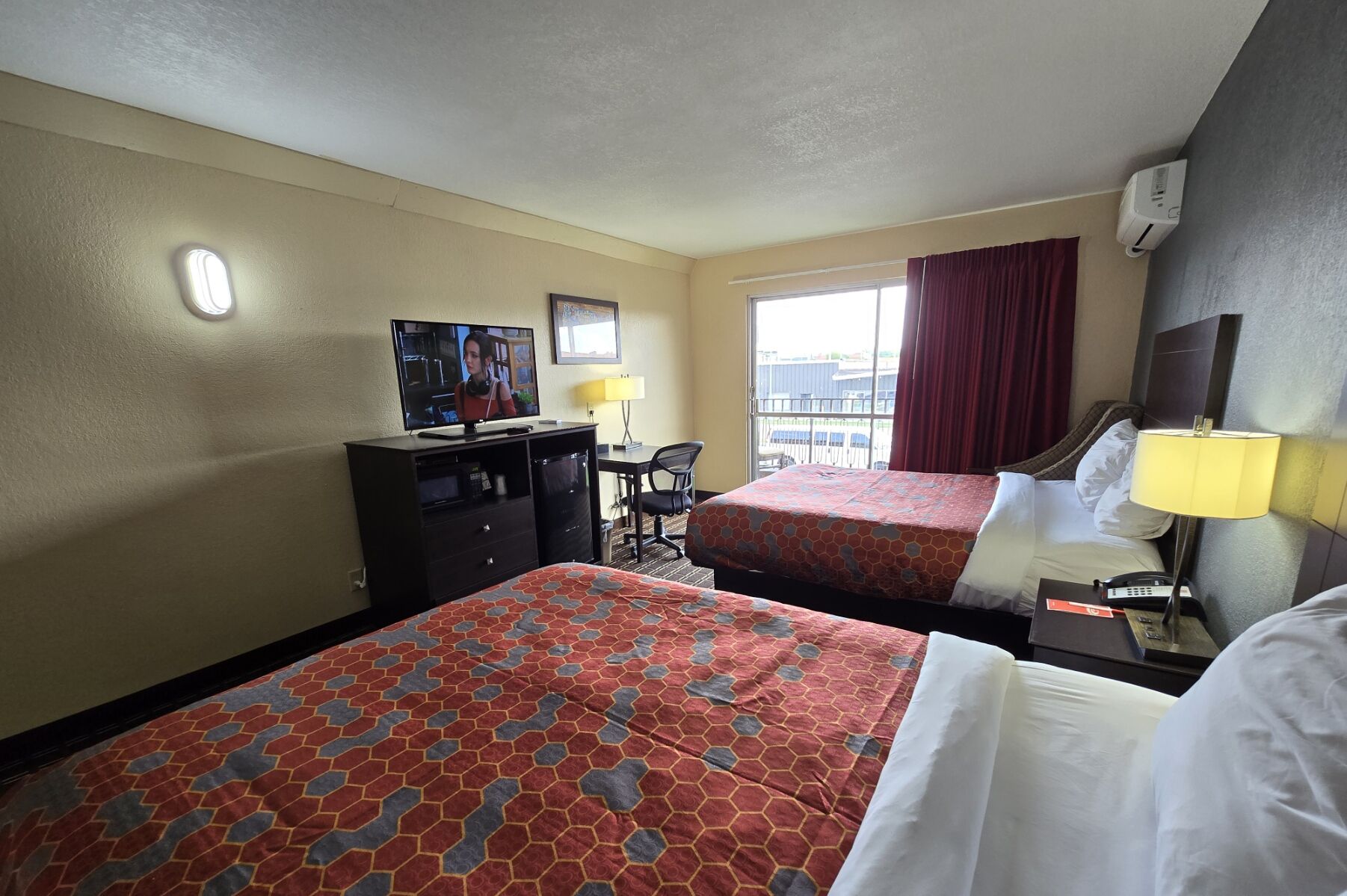 A hotel room with two beds, a desk with a computer, a TV, and a window with curtains.