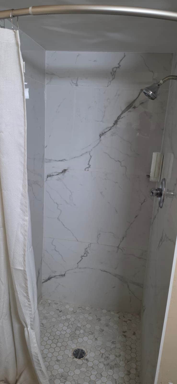 A shower with a marble wall and a hexagonal tile floor.