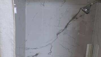 A shower with a marble wall and a hexagonal tile floor.