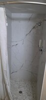 Ducha con pared de mármol y suelo de baldosas hexagonales.