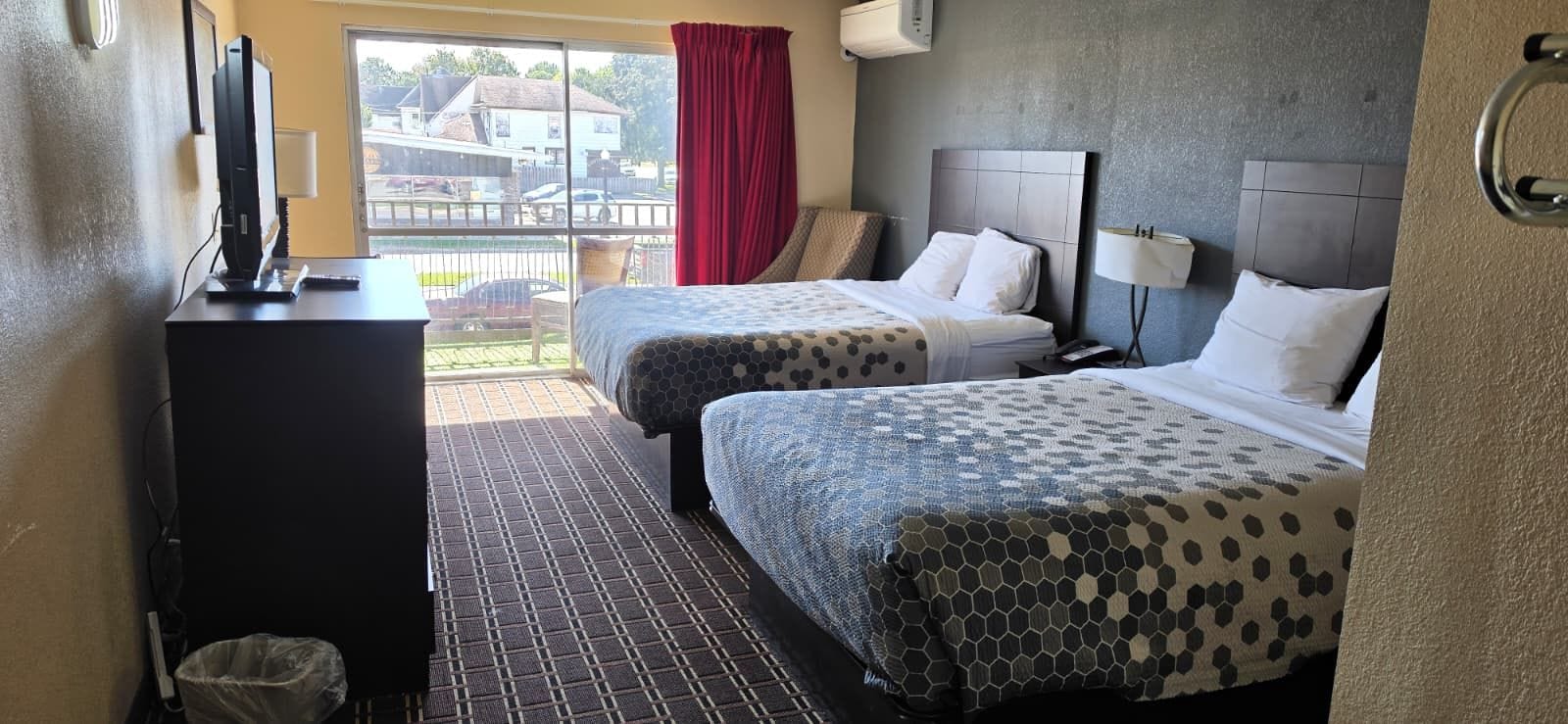 Habitación de hotel con dos camas, un escritorio con computadora, un cesto de basura y una ventana con vista al exterior.