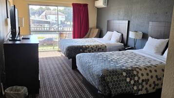 Habitación de hotel con dos camas, un escritorio con computadora, un cesto de basura y una ventana con vista al exterior.