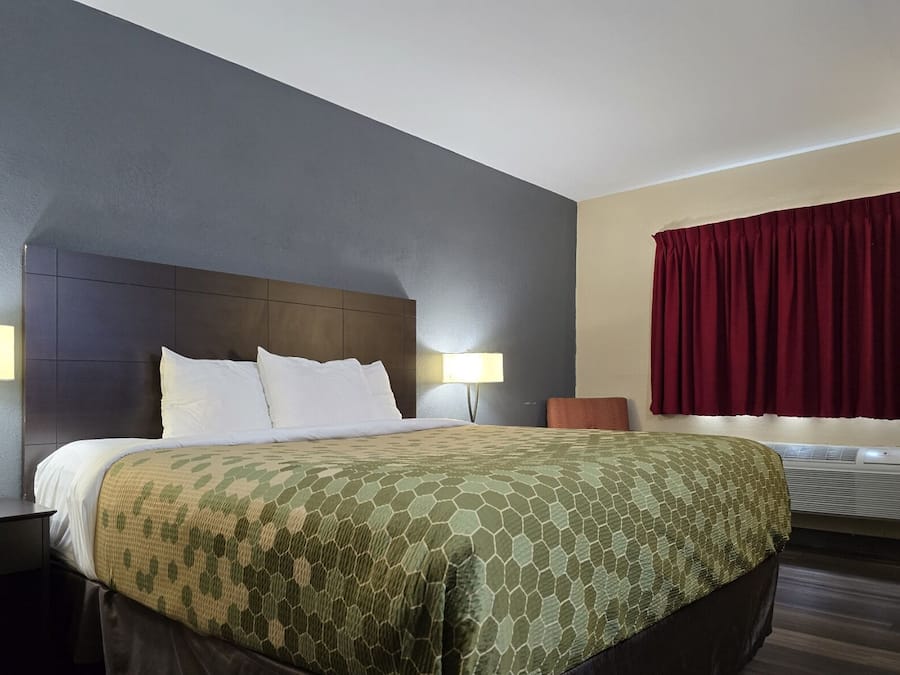 Une chambre d’hôtel avec un grand lit, deux lampes de chevet, un rideau rouge et un appareil de climatisation.