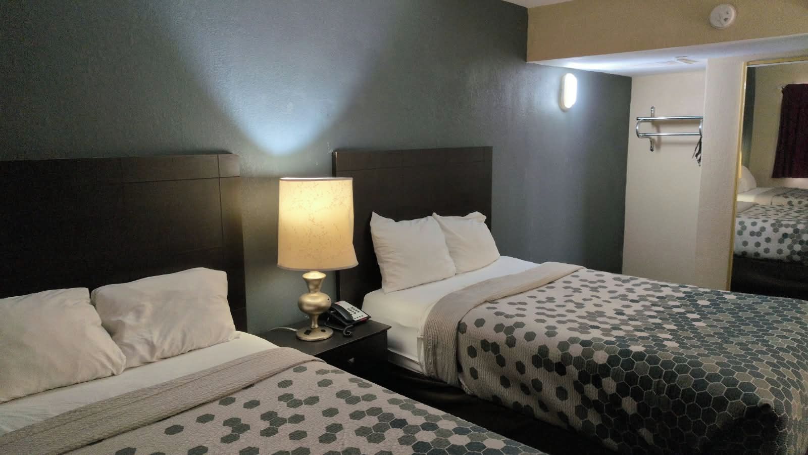 A hotel room with two beds, a bedside table with a lamp, and a mirror.