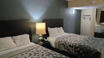 A hotel room with two beds, a bedside table with a lamp, and a mirror.