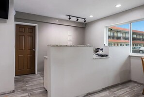 A hotel room with a wooden door, a small kitchenette, a window with a view of buildings, and a ceiling light fixture. - Stay Mason City (Mason City)