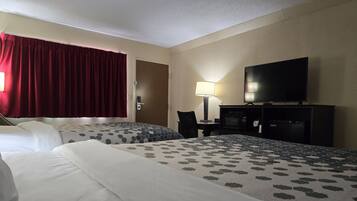 A hotel room with two beds, a television, a desk with a lamp, and a microwave.