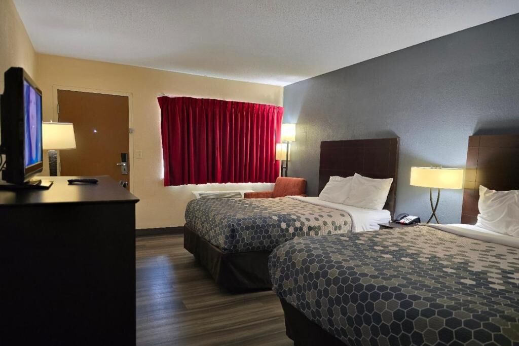 A hotel room with two beds, a TV, a desk, and a red curtain.