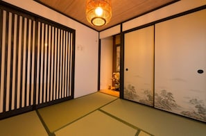 A traditional Japanese room with tatami flooring, sliding doors, and a hanging lamp.