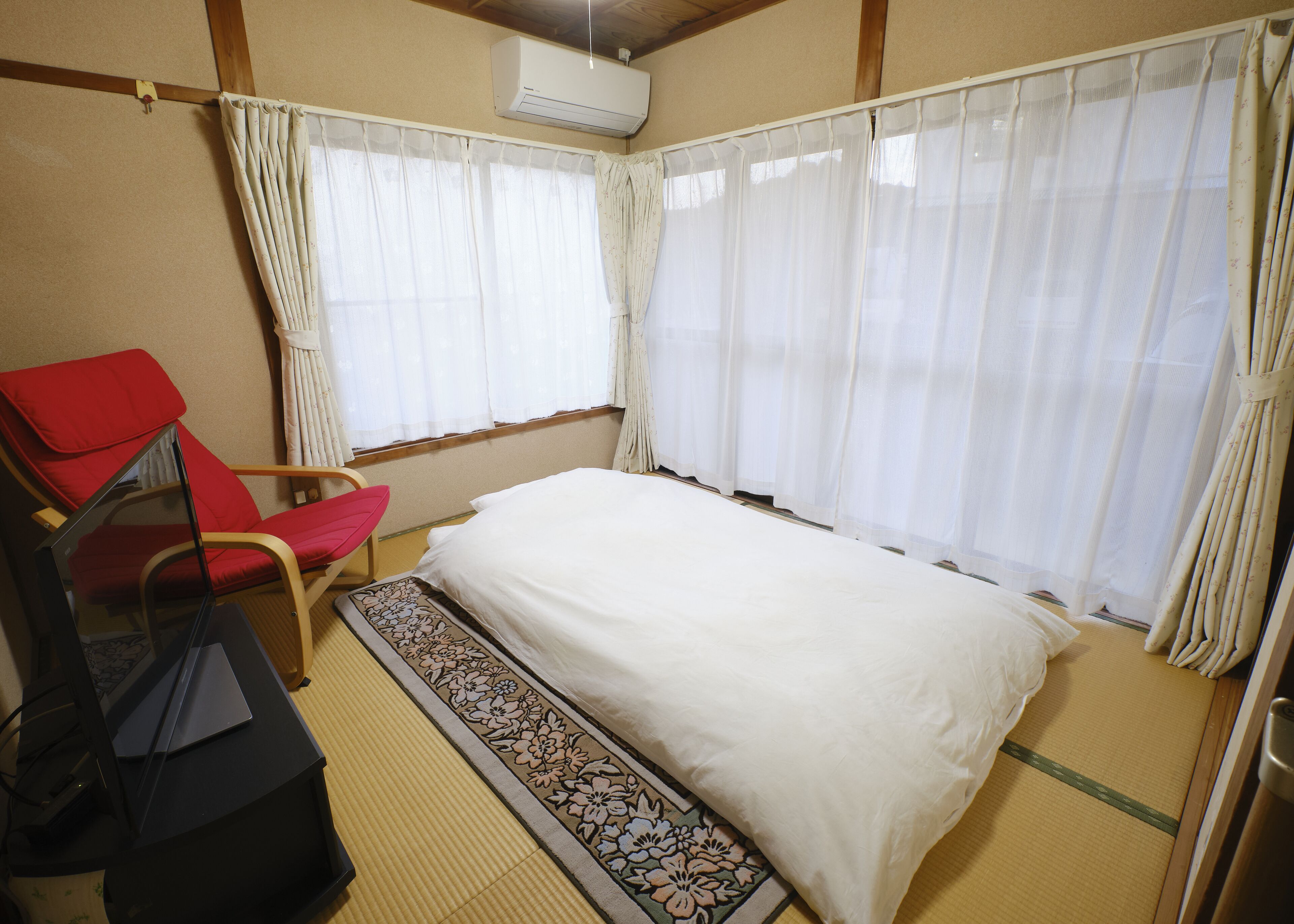 A room with a bed, a red chair, a small table, and a window with curtains.