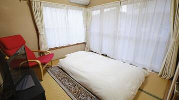 A room with a bed, a red chair, a small table, and a window with curtains.