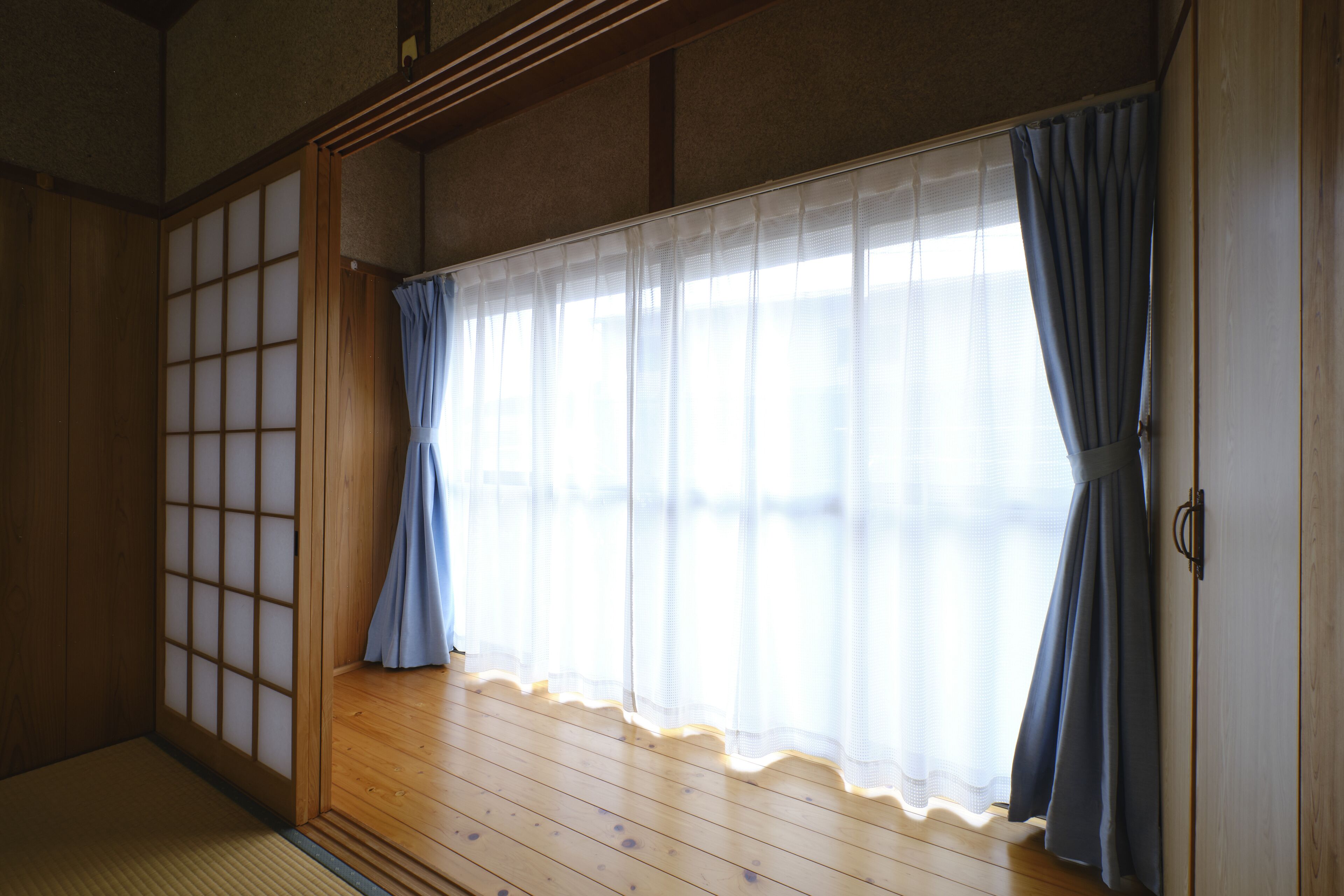 Una habitación japonesa tradicional con suelo de tatami, paneles shoji y un puertas correderas con cortinas azules.