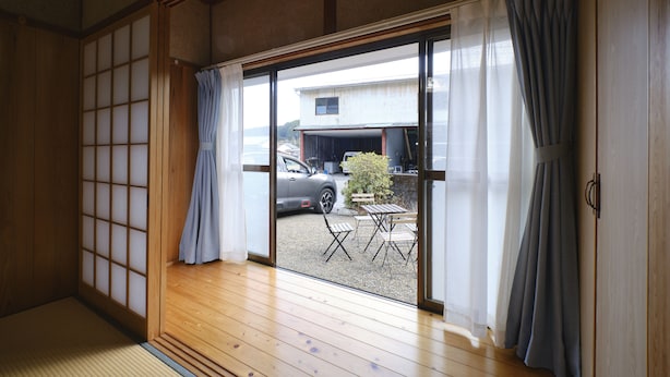 A traditional Japanese room with tatami flooring, sliding doors, and a view of a car and outdoor furniture. - Vacation rentals -un- (Nachikatsuura)