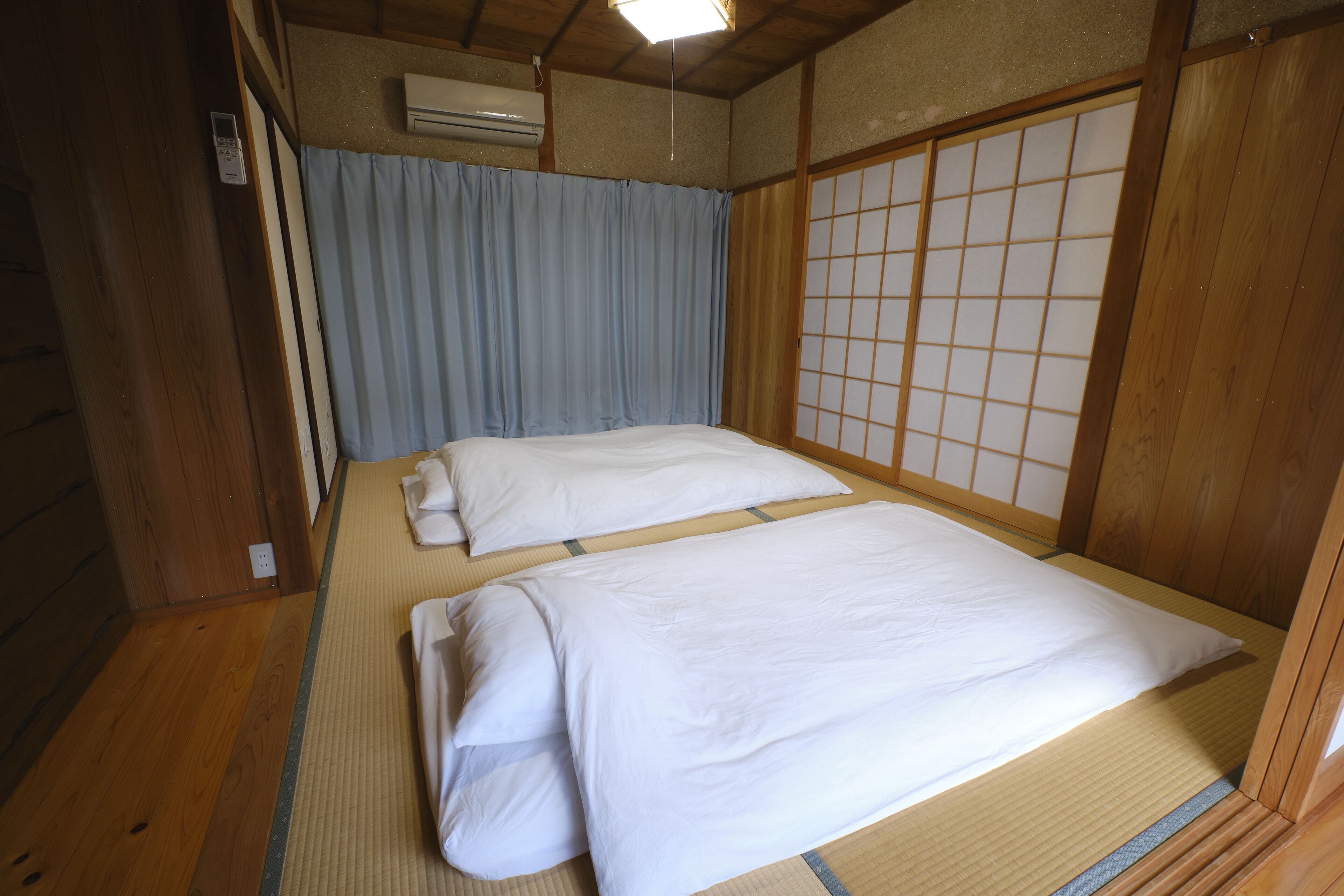 A traditional Japanese-style room with tatami flooring, two beds with white bedding, a sliding shoji screen, and an air conditioning unit.