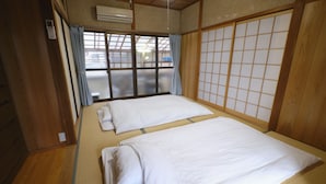 A traditional Japanese room with tatami flooring, two beds with white bedding, sliding doors, and a view through a large window. - Vacation rentals -un- (Nachikatsuura)