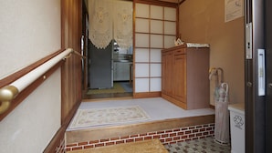 A narrow hallway with a wooden floor, a mat at the entrance, a sliding door with a decorative curtain, and a small kitchen area visible through the door. - Vacation rentals -un- (Nachikatsuura)