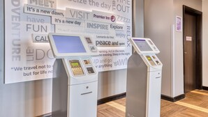 A hotel lobby with a large motivational poster, two self-service kiosks, and a door to the right. - Premier Inn Isle of Wight Sandown - Seafront (Sandown)