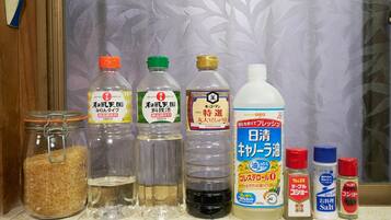 A shelf with various food items including a jar of sugar, bottles of soy sauce, a bottle of rice vinegar, a bottle of salt, and two bottles of pepper.