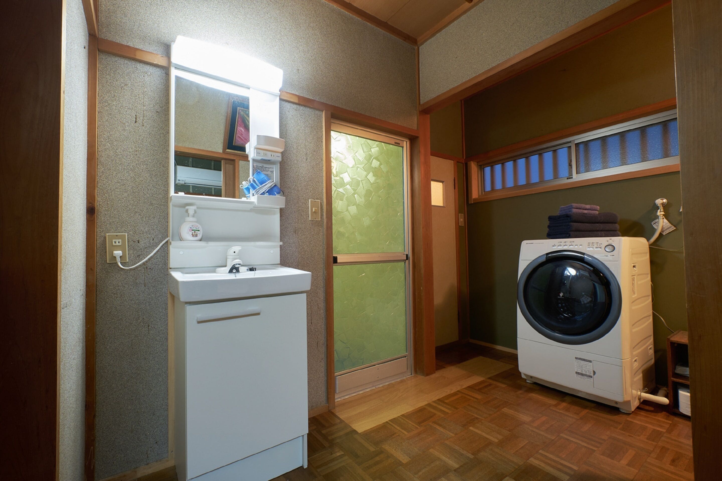 A laundry room with a washing machine, a dryer, a mirror, and a window with blinds.