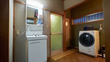 A laundry room with a washing machine, a dryer, a mirror, and a window with blinds.
