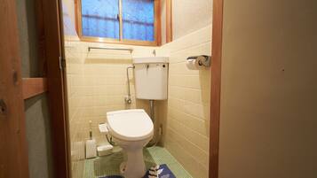 A small bathroom with a toilet, a window, and a blue patterned mat on the floor.