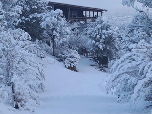 Paisaje nevado con una casa que tiene un balcón y un sendero que la lleva hasta allí.