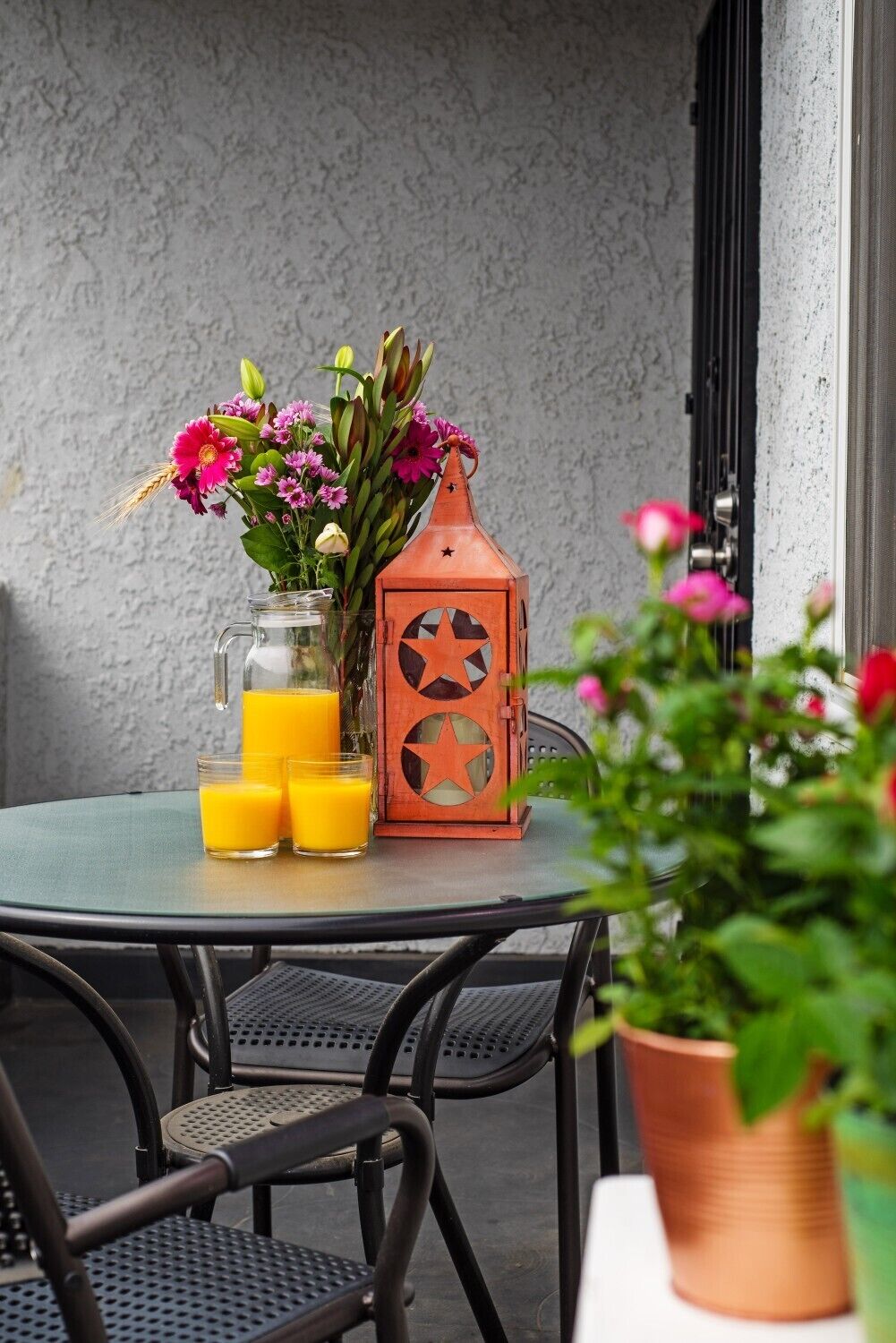 Una mesa redonda con una jarra de vidrio, tres vasos de jugo de naranja y un farol de terracota con diseños de estrellas.