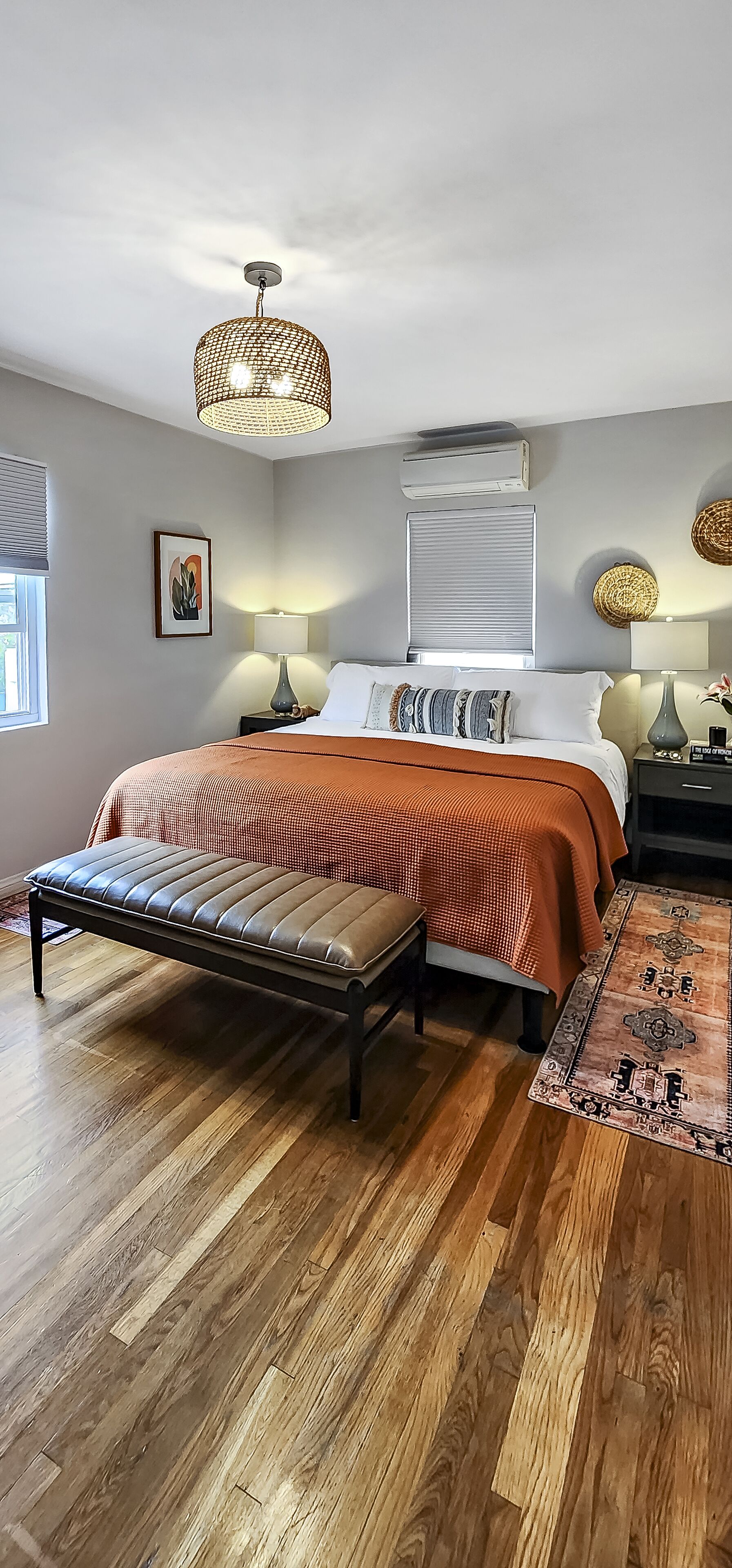 A bedroom with a bed, bedside lamps, a bench, a rug, and a ceiling light fixture.