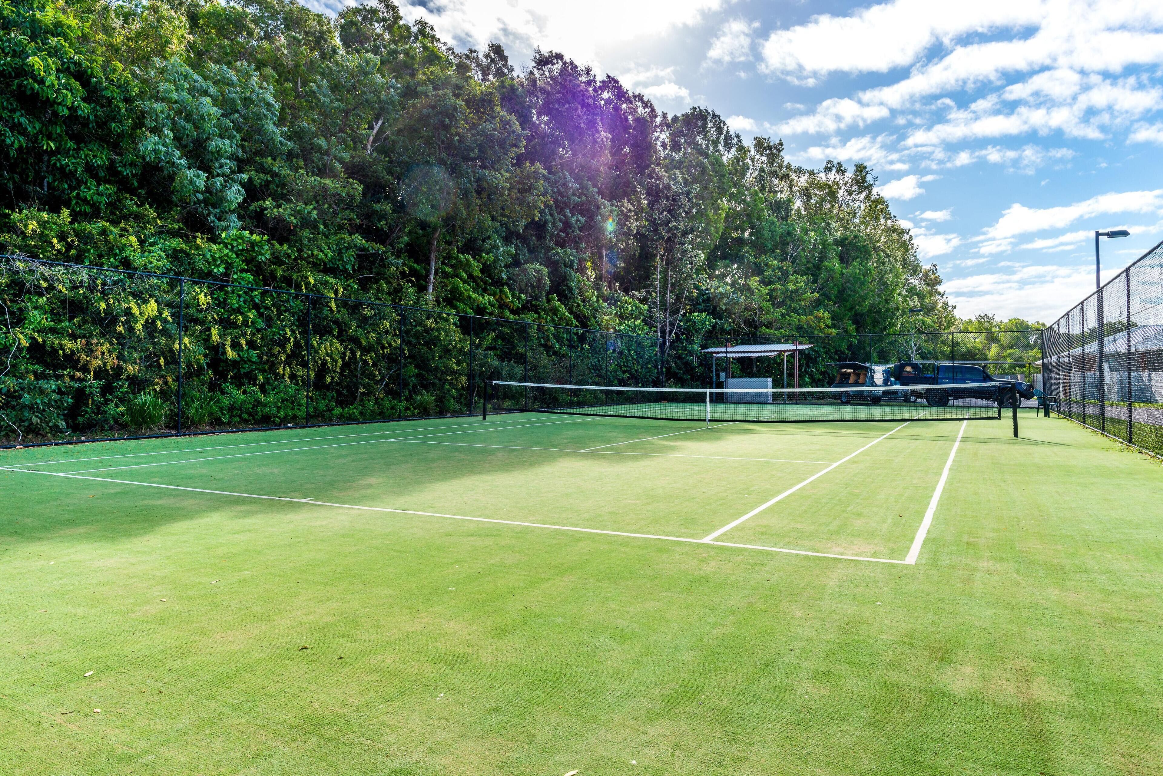 Een tennisbaan omgeven door dichte bomen en een heldere lucht.